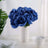 Blue artificial roses in a white vase on a table.