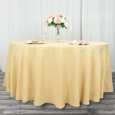 Round table set with a beige tablecloth, flowers, and glassware for dining.
