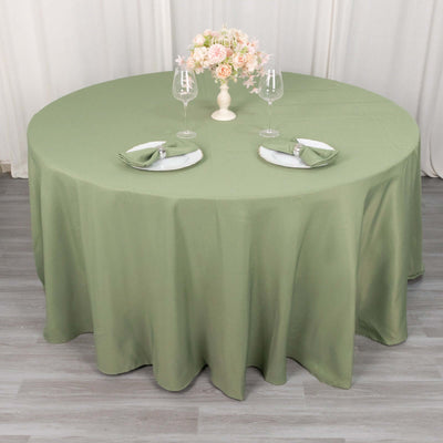 Round green tablecloth draped over a table set with plates and glasses.