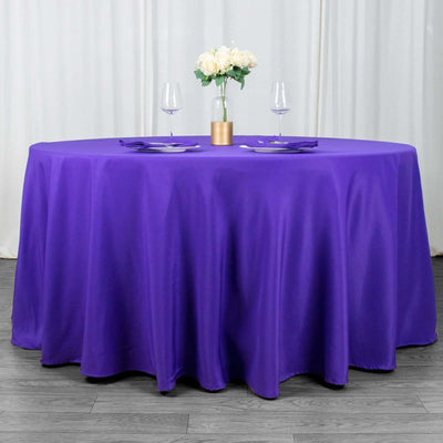 Purple round tablecloth with elegant floral centerpiece and wine glasses.