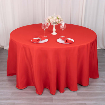 Red round tablecloth draped over a table set for two with floral centerpiece.