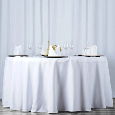Elegant round dining table set with white linens and glassware.