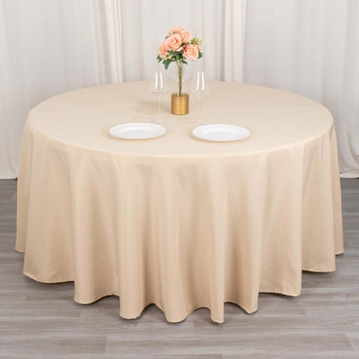 Beige round tablecloth draped over a table with plates and floral centerpiece.