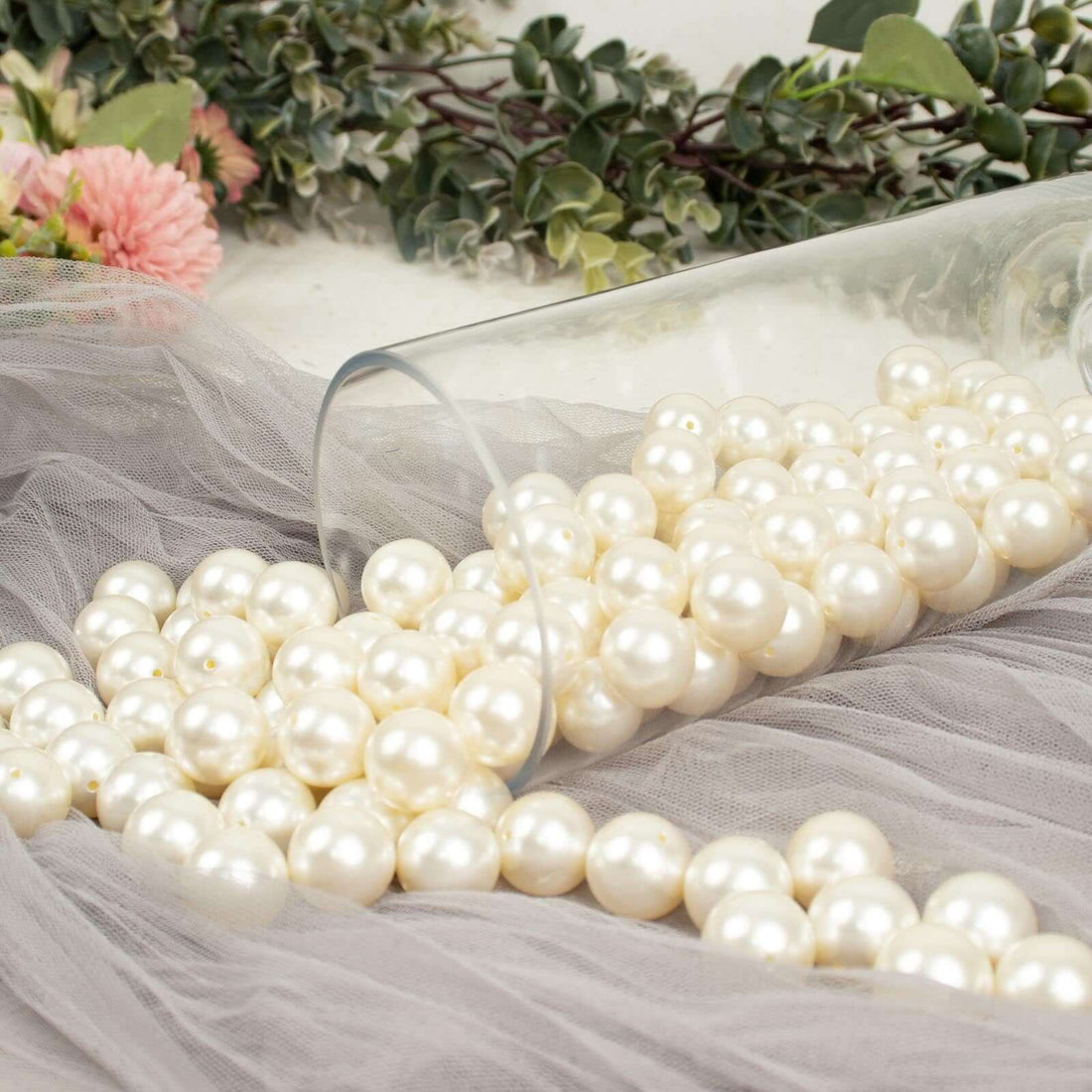 White faux pearls spilling from a glass vase on soft fabric.
