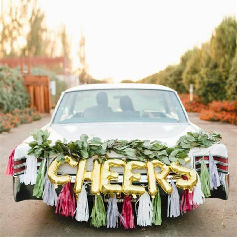 Decorative car with "CHEERS" balloons and greenery for a celebration.