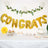 Gold "Congrats" balloons with festive decorations and treats at a celebration.