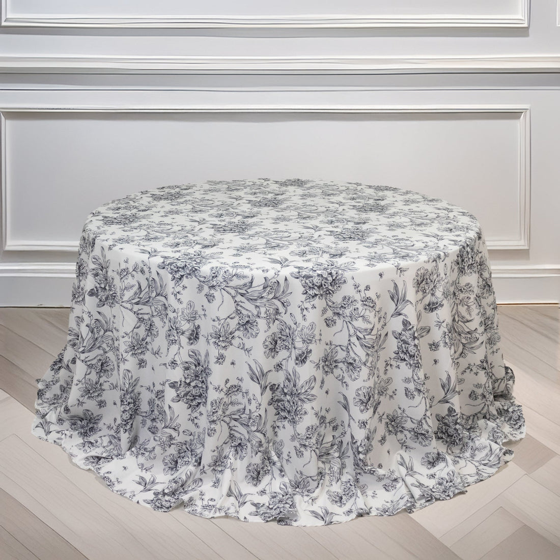 Floral round tablecloth on a wooden floor against a white wall.