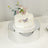 White cake decorated with butterfly toppers on a reflective cake stand.