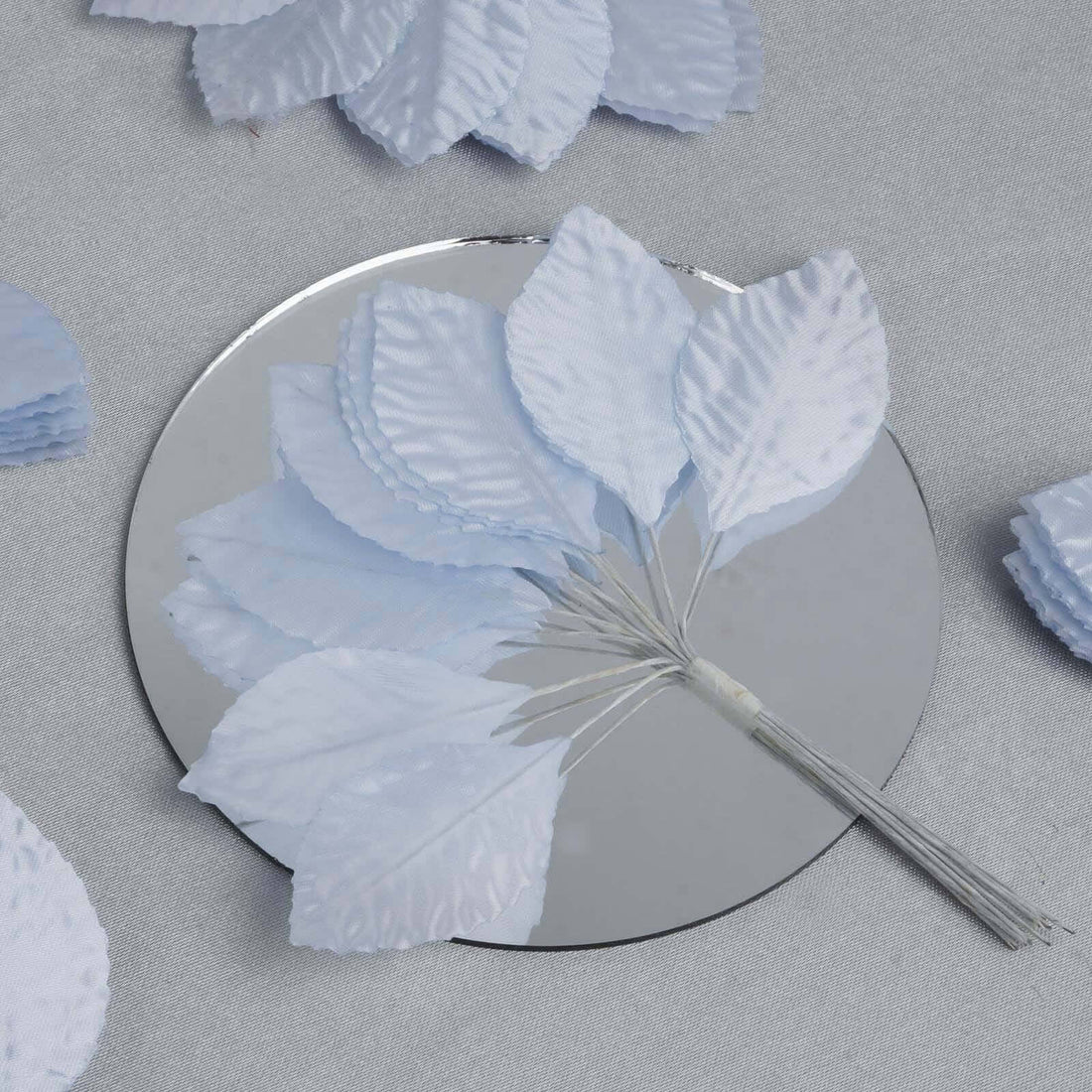 Light blue artificial leaves arranged on a mirror surface.