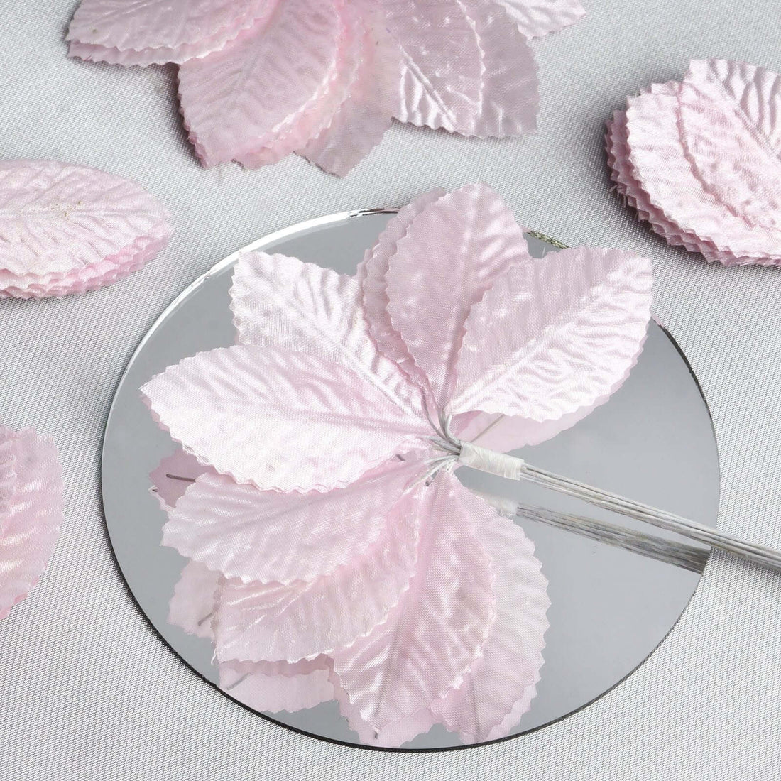 Pink decorative fabric leaves on a circular mirror surface.