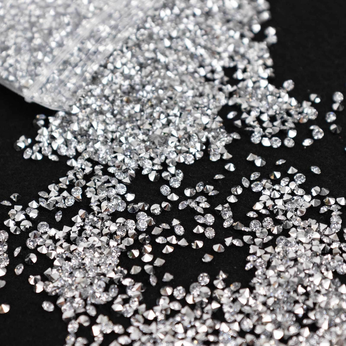 Silver rhinestones scattered on a black surface, showcasing their sparkle and shape.