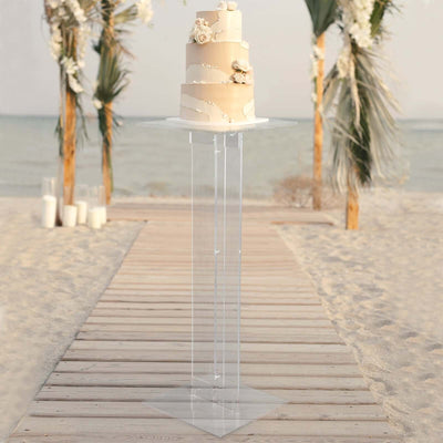 Elegant wedding cake on a clear stand by the beach.