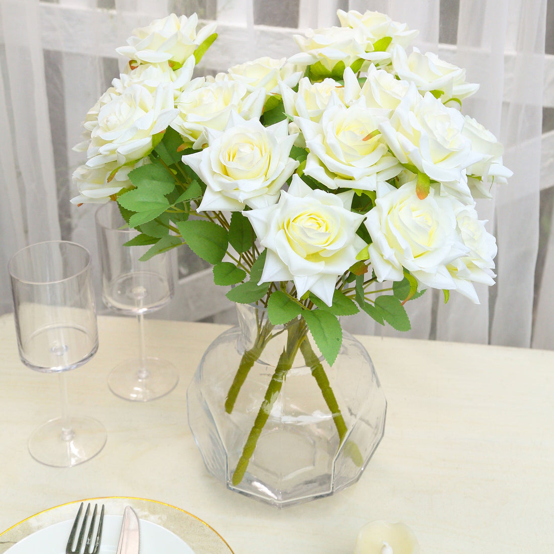 Artificial white roses bouquet in a clear vase on a table.