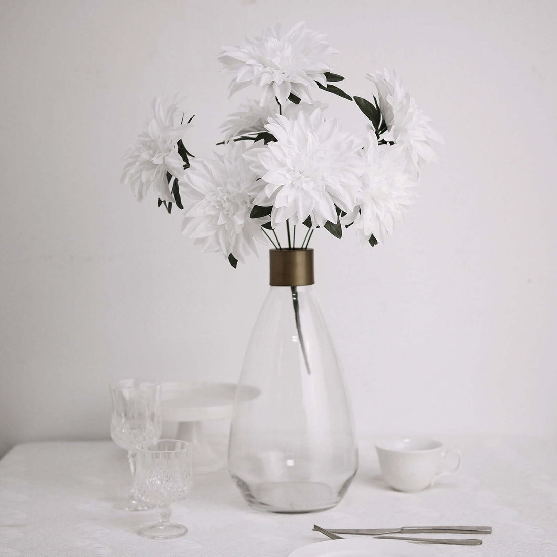 White faux flowers in a clear glass vase on a table setting.