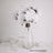White faux flowers in a clear glass vase on a table setting.