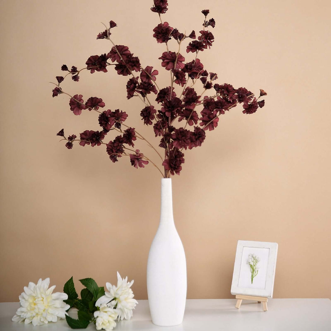 Elegant maroon flower arrangement in a white vase on a neutral background.