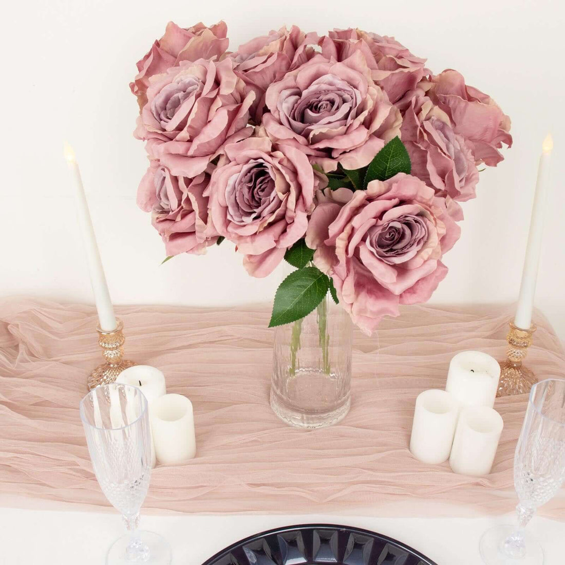 Bouquet of pink roses in a glass vase on a table with candles and crystal glasses.