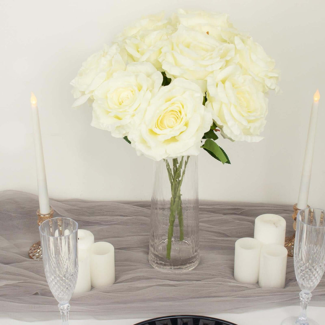 White rose bouquet in a glass vase with candles on a table.