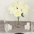 White rose bouquet in a glass vase with candles on a table.