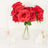Red roses in a glass vase with candles on a white table.