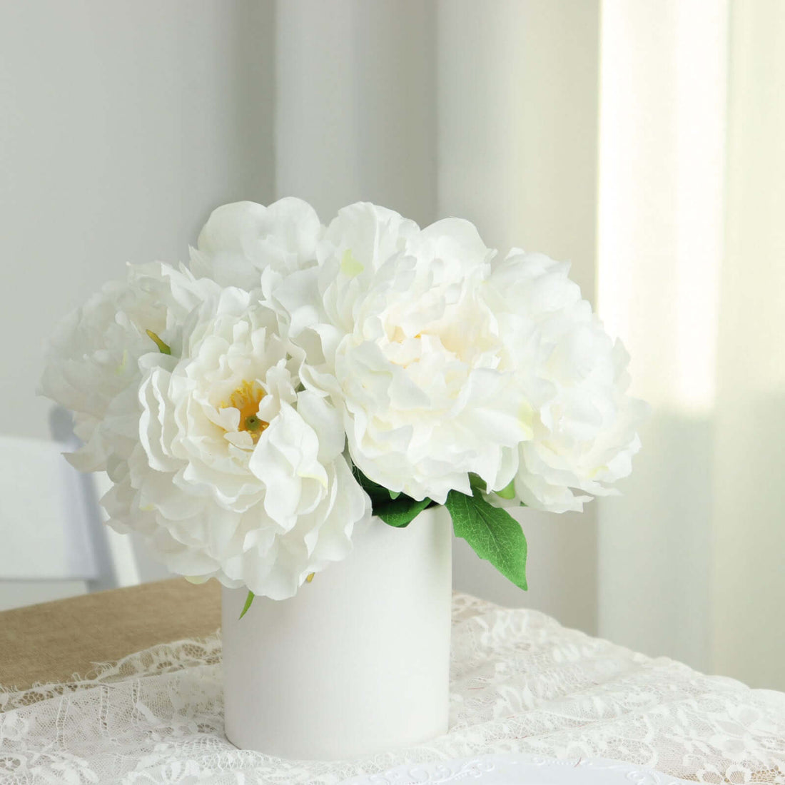 White peony flowers in a simple white vase on a lace tablecloth.