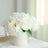 White peony flowers in a simple white vase on a lace tablecloth.