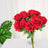 Bouquet of red artificial roses in a clear vase with green leaves.