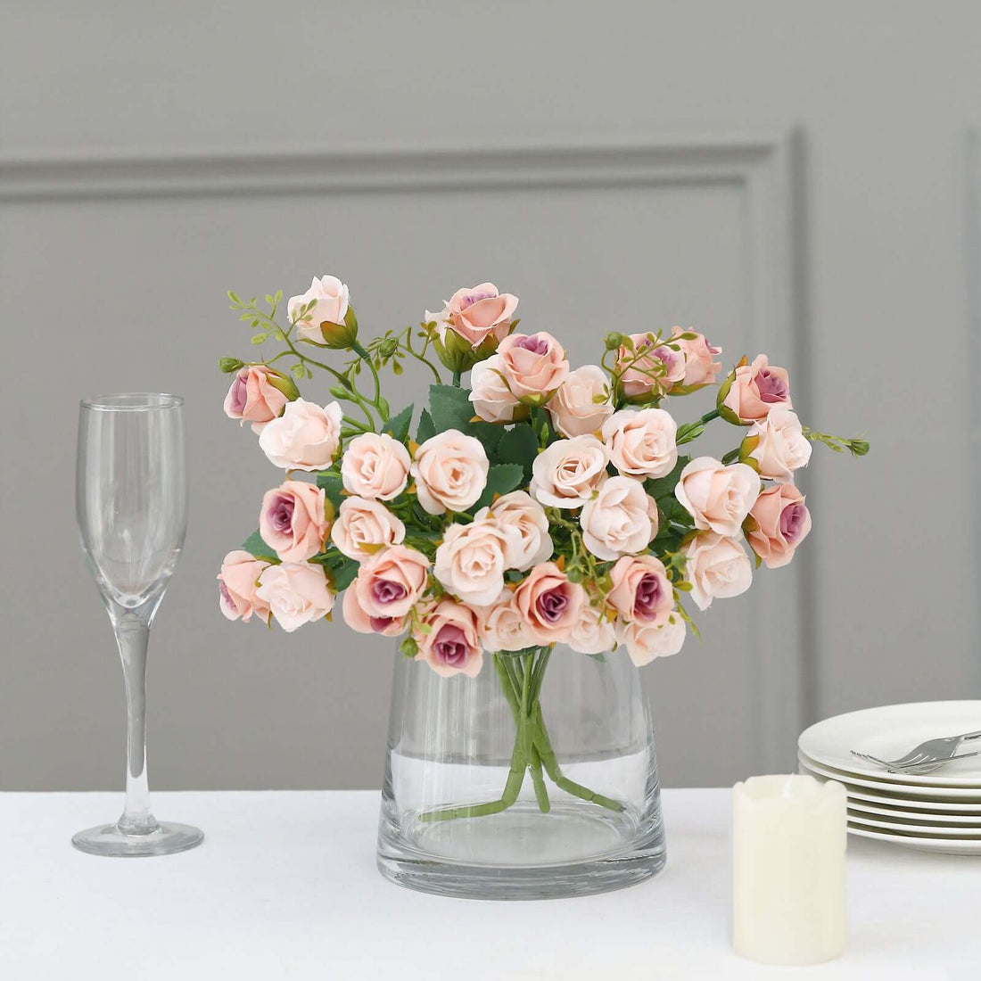 Pink and purple artificial flower bouquet in a glass vase on a table.