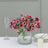 Pink roses in a clear vase on a table with dinnerware and a glass