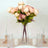 Pink peony bouquet in a clear vase with candles on a table setting.