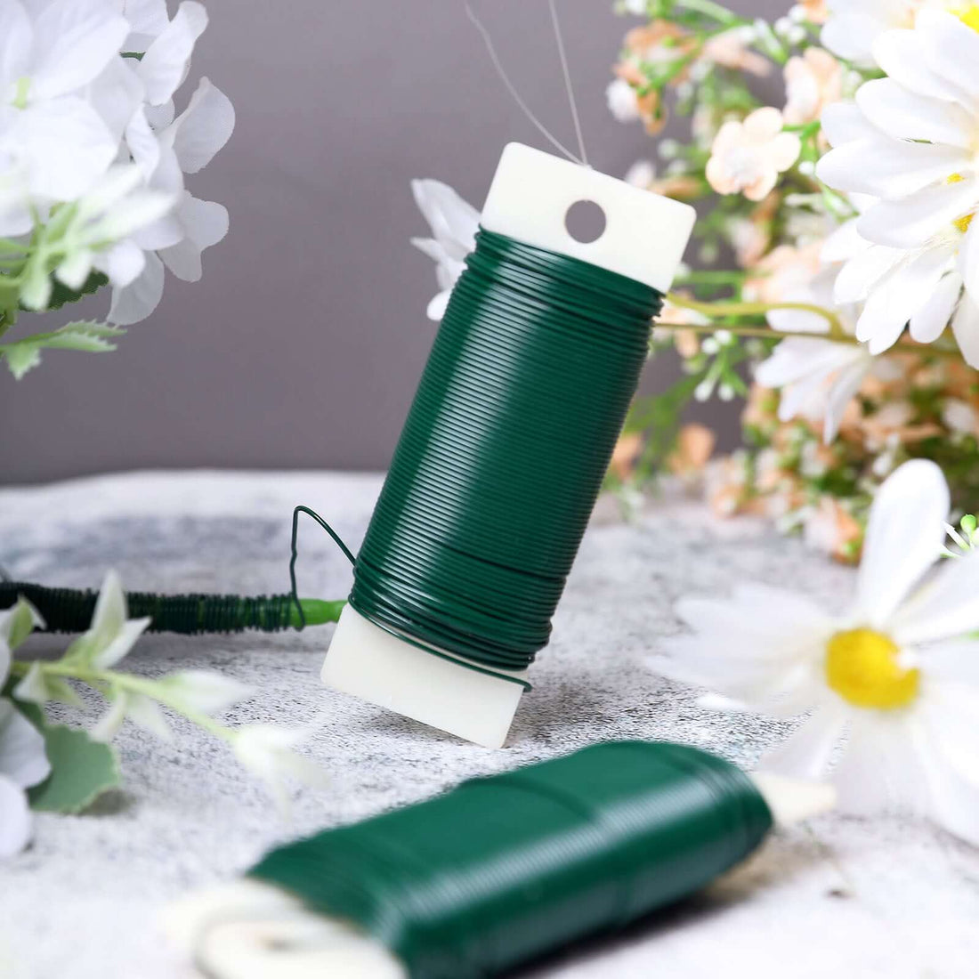 Green floral wire spool with white label, surrounded by flowers.