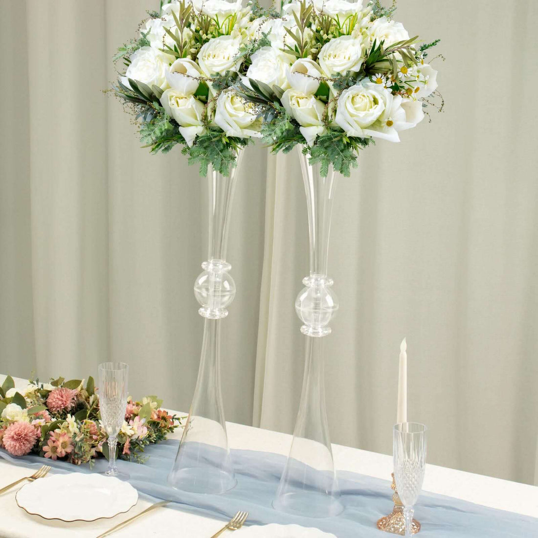 Elegant floral arrangements in tall glass vases on a decorated table setting.