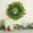 Green foliage wreath with candles and glass on a marble surface.