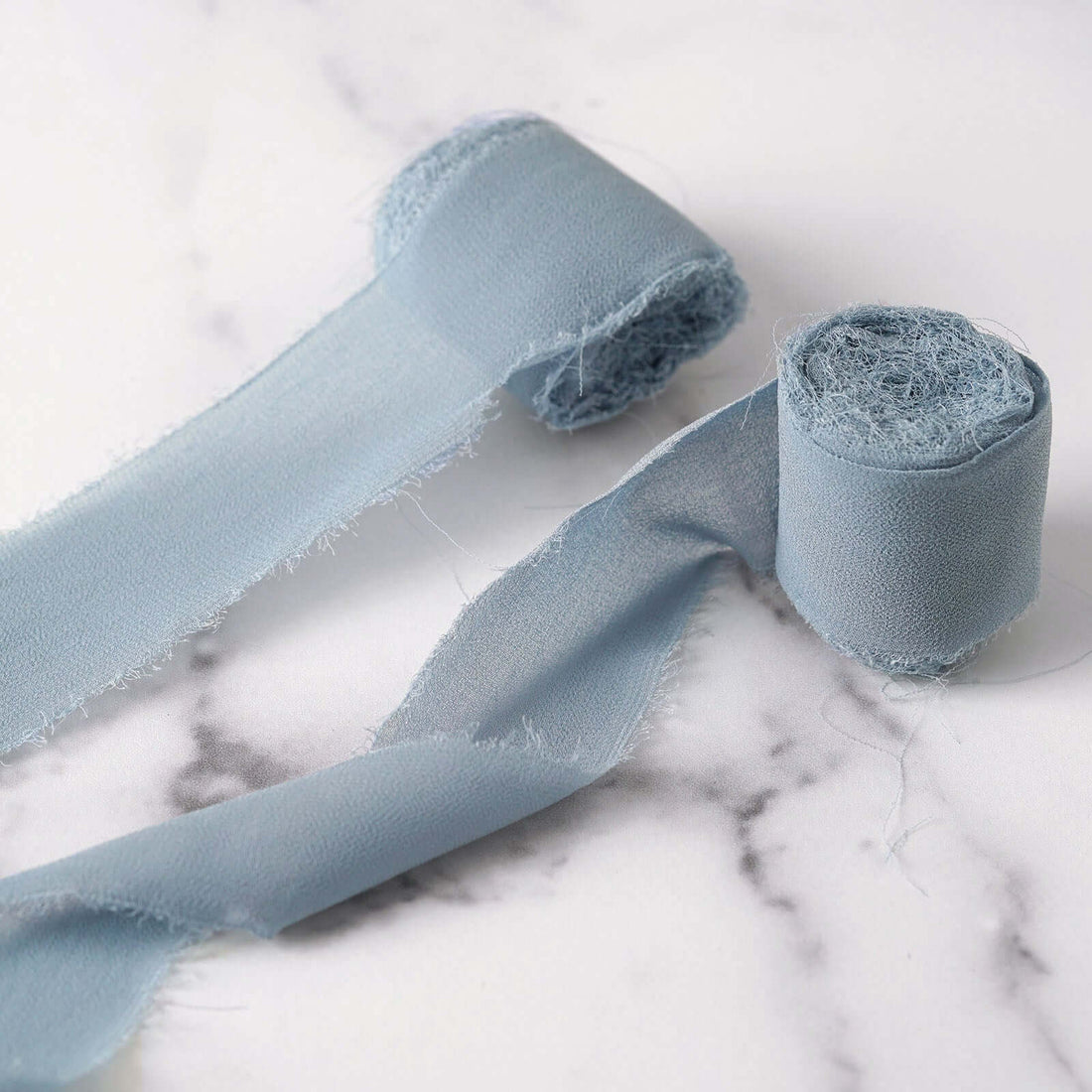Light blue fabric ribbon rolls on a marble surface.