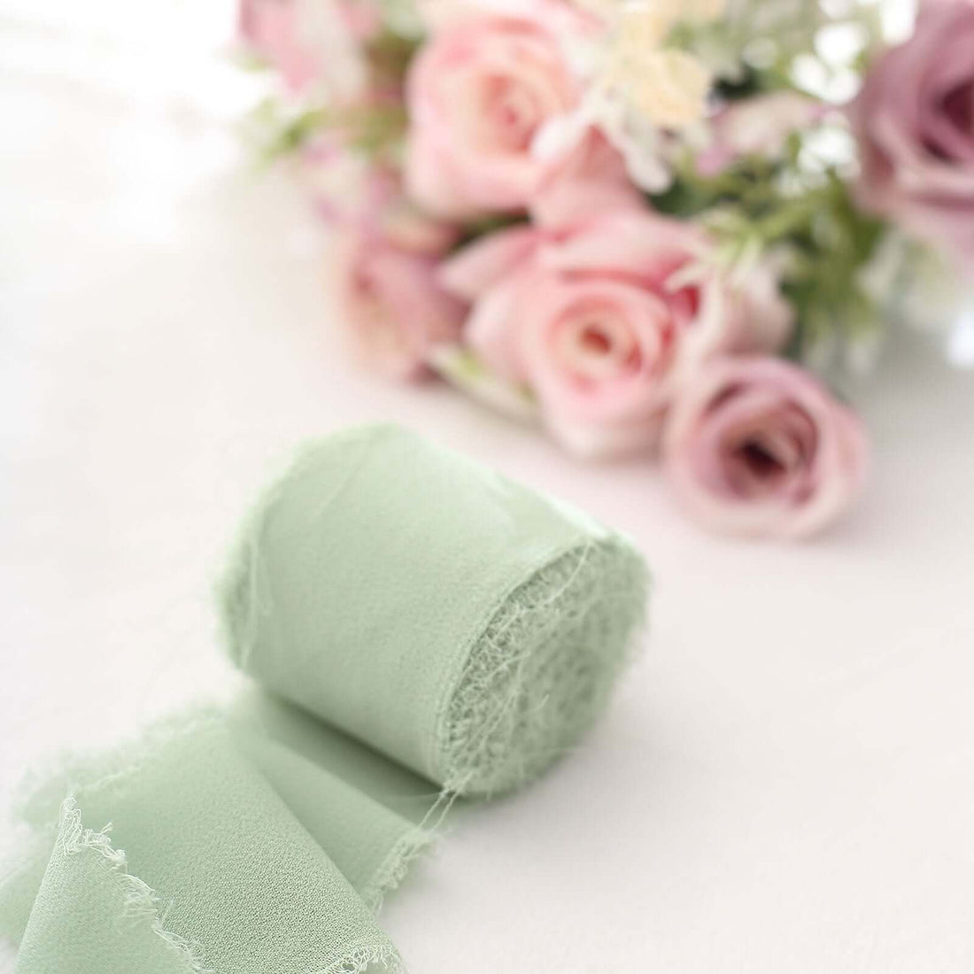 Mint green fabric roll with soft texture, blurred pink roses in background.