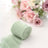 Mint green fabric roll with soft texture, blurred pink roses in background.