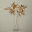Gold leaf branches in a clear vase on a minimalist table.