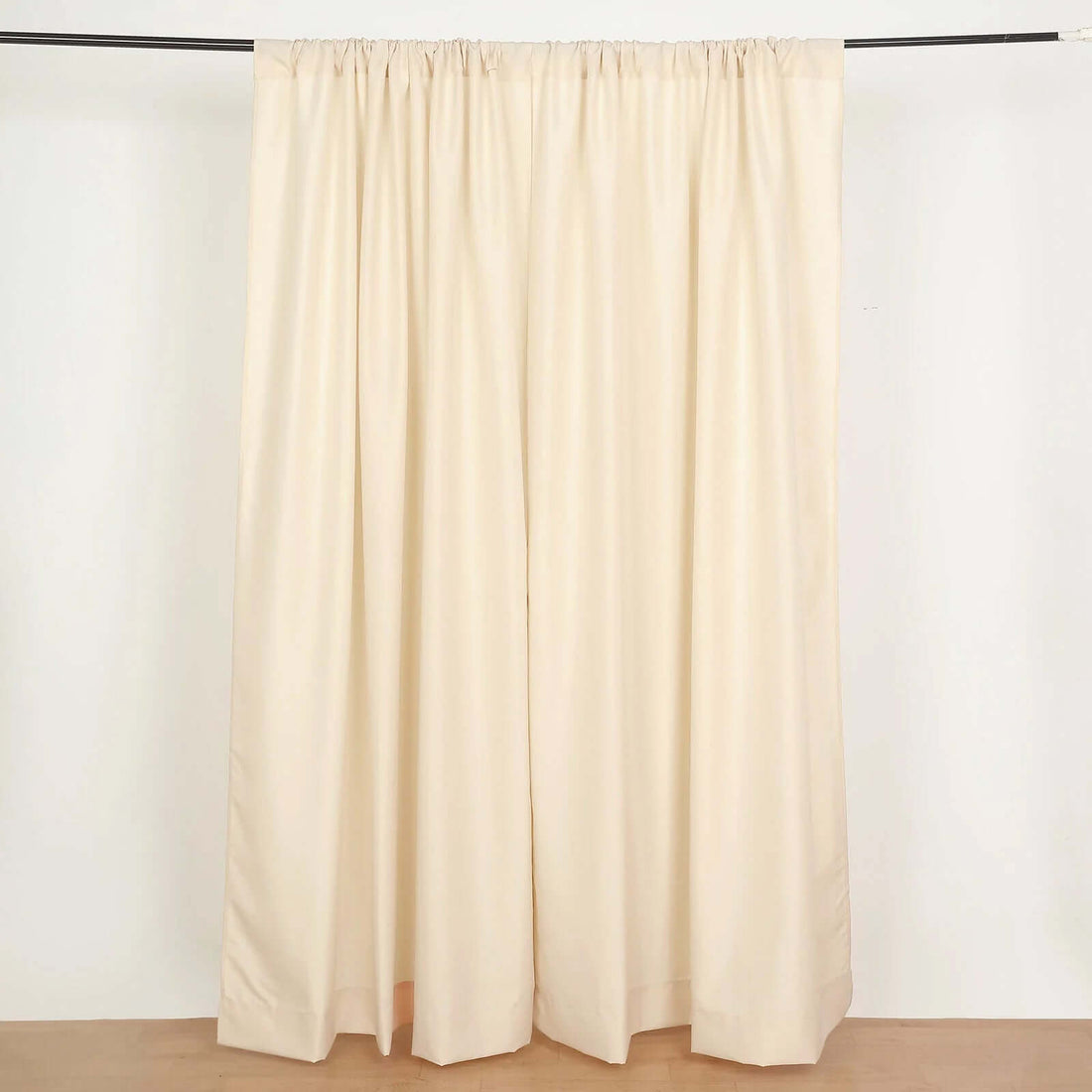 Beige fabric curtains hanging on a rod against a plain background.