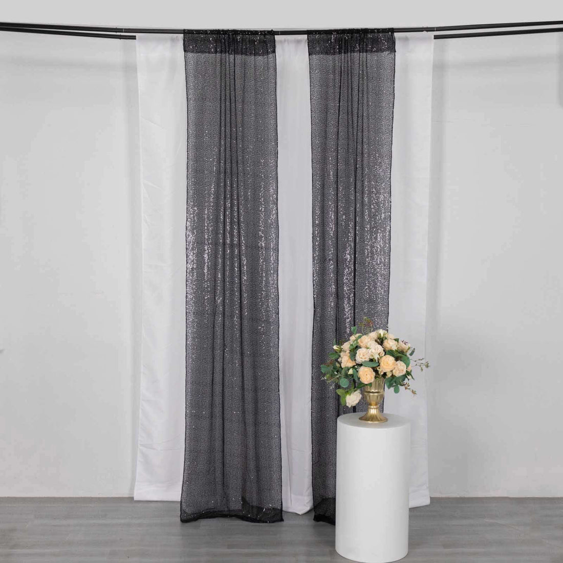 Black sequin curtain draped with white fabric and a floral arrangement in a vase.