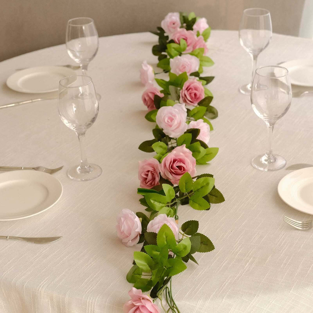 Pink rose flower garland centerpiece for table settings with glassware and plates.