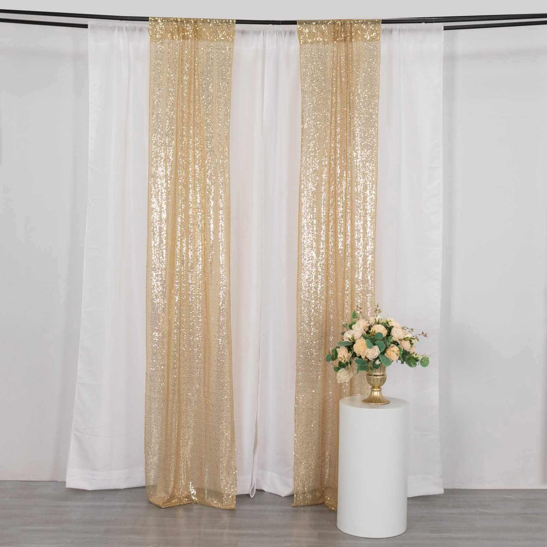 Gold sequin curtain drapes with white backdrop and floral arrangement.