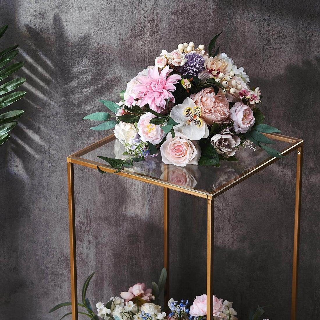 Elegant floral arrangement in a glass display stand against a textured wall.