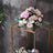 Elegant floral arrangement in a glass display stand against a textured wall.