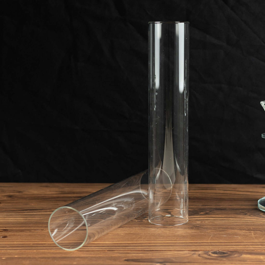 Clear glass tube vase on wooden table, one upright and one lying down.