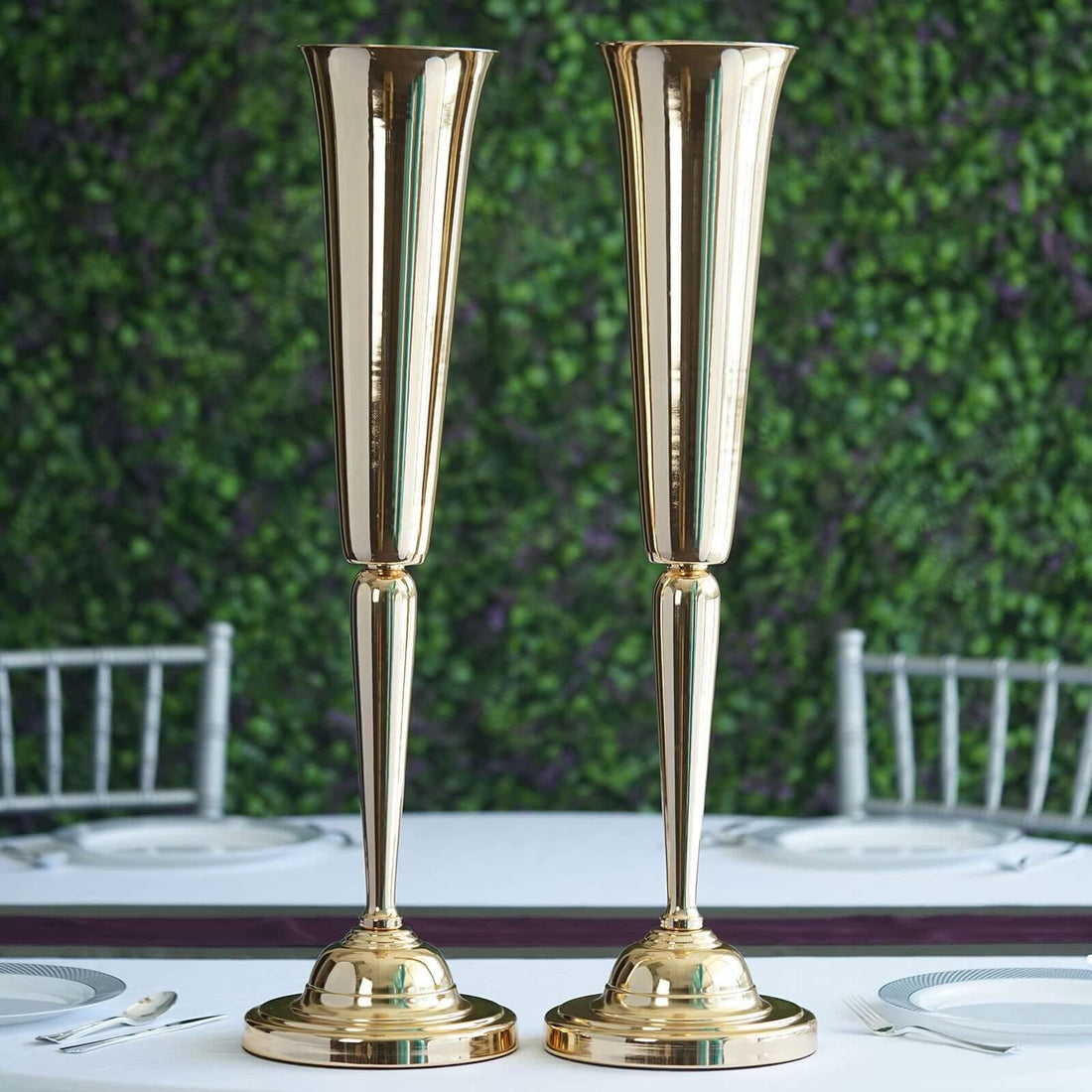 Elegant gold vases on a dining table with greenery backdrop.