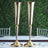 Elegant gold vases on a dining table with greenery backdrop.