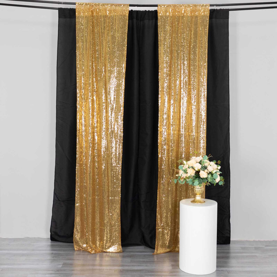 Gold sequin backdrop curtains with a floral arrangement on a white pedestal.