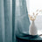 Sheer teal curtain draping elegantly beside a minimalist vase and dried flowers.