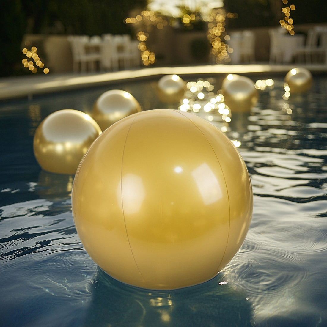 Gold inflatable beach balls floating in a pool with blurred lights in the background.