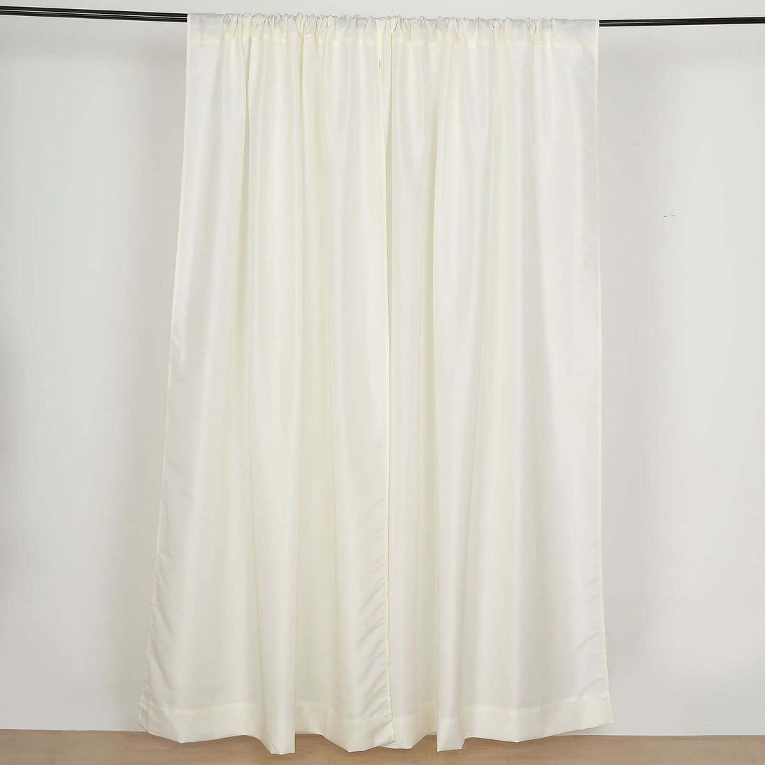 Cream curtain panel with a smooth finish hanging on a curtain rod.